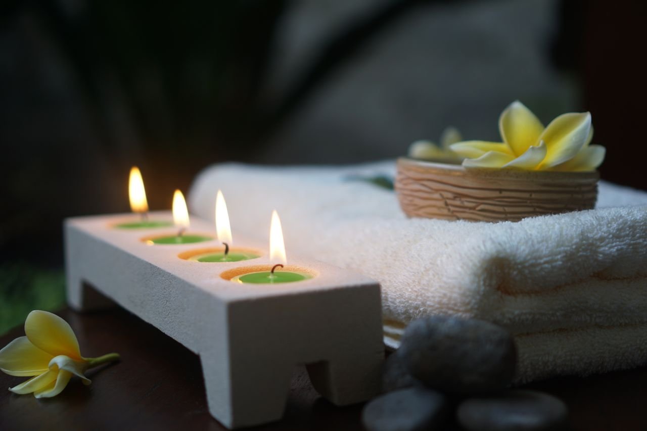 hero-img-02 Relaxing spa scene featuring flickering candles, soft towels, and fresh flowers.