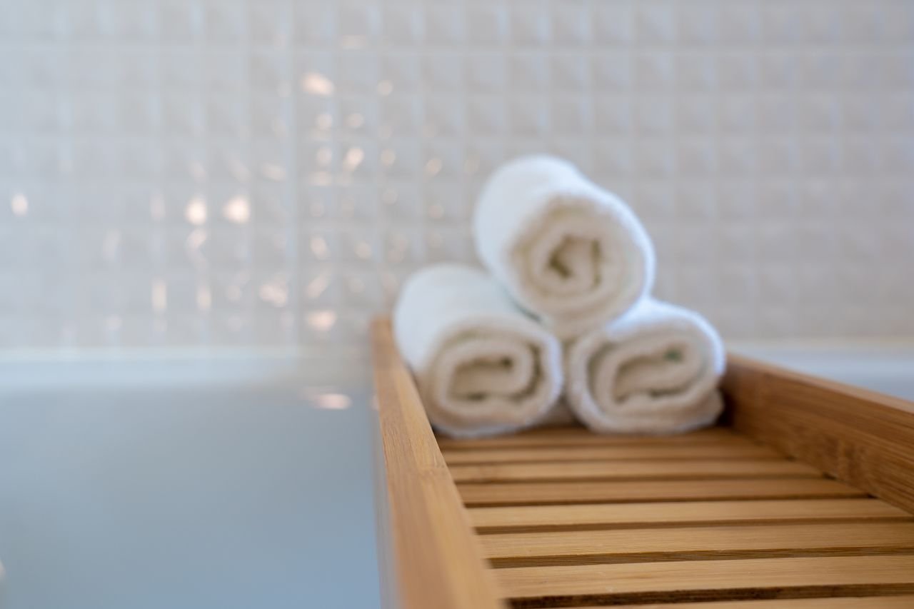 why-choose-us A close-up of rolled white towels on a wooden bath tray in a modern bathroom.
